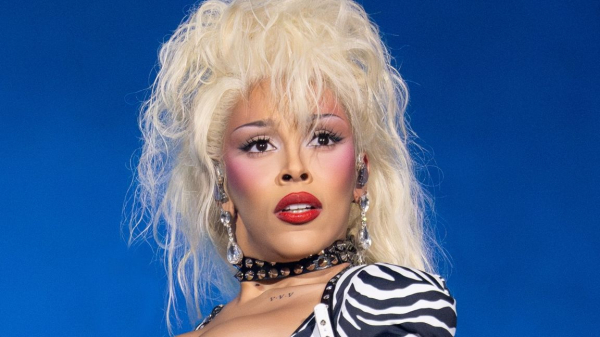 Doja cat wearing big bleach blonde hair against a blue background
