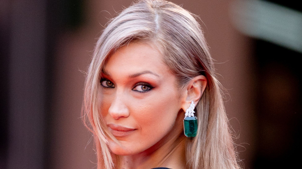 Bella Hadid poses on the runway in a black dress and emerald earrings. Her hair is worn down.